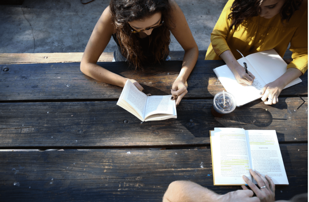 three students at a picnic table two read as one takes notes