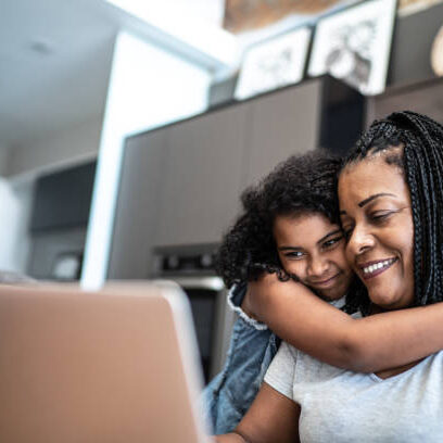 Mature woman working from home and being embraced by daughter