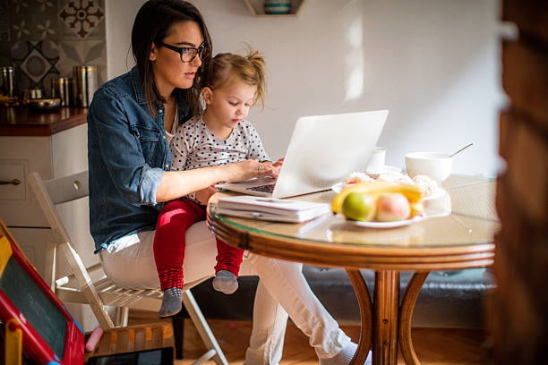 mother with daughter on lap working on computer at the kitchen table