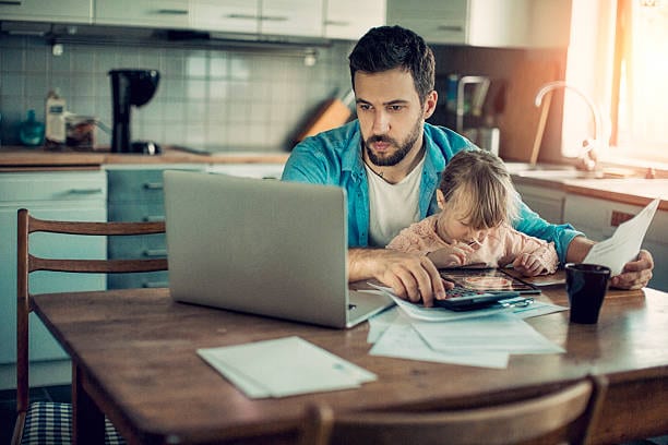 Father working on a computer with daughter on his lap in the kitchen