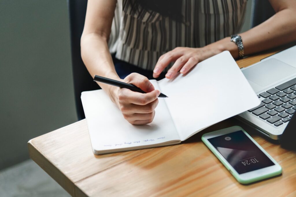 woman taking notes at a desk in front of a laptop