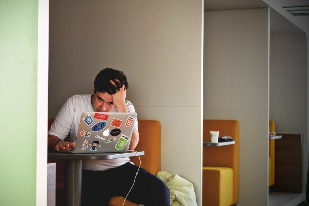 a frustrated man works on a laptop in a booth